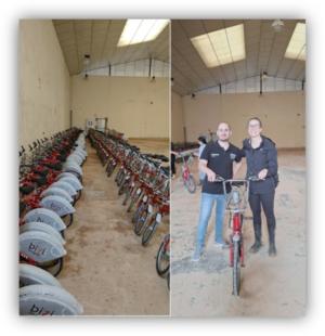 Interior de una nave con filas de bicicletas aparcadas y, a la derecha, dos personas posando junto a una bicicleta.