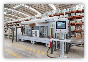 Máquina industrial automatizada en un almacén con estanterías llenas de cajas organizadas.