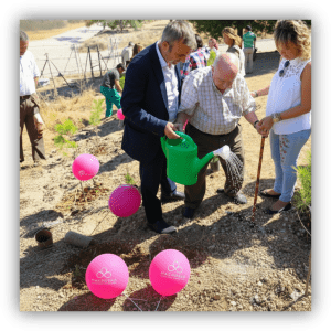 Personas participan en una actividad de plantación de árboles, regando un plantón en un entorno natural con globos rosas alrededor.