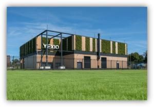 Edificio industrial moderno con fachada vegetal y paneles de madera, rodeado de una zona ajardinada.