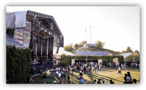 Recinto de festival al aire libre con un escenario principal, asistentes en una zona de césped y paneles solares instalados en distintas áreas del espacio.