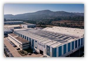 Vista aérea de una planta industrial de Gestamp con paneles solares instalados en la cubierta, rodeada de zonas industriales y montañas