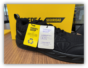 Calzado de seguridad negro fabricado con materiales reciclados, presentado junto a etiquetas informativas y su caja de embalaje.