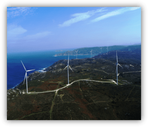 Vista aérea de varios aerogeneradores instalados en una zona costera con el mar al fondo.
