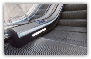 Primer plano de una escalera mecánica con iluminación lateral y señalización de seguridad en el pasamanos.