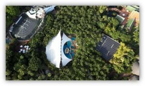Vista aérea de un complejo rodeado de abundante vegetación tropical, con edificios equipados con paneles solares en las cubiertas y una zona central cubierta por una estructura tensada blanca.