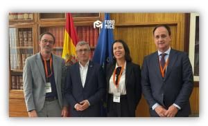 Cuatro personas posan en una biblioteca frente a las banderas de España y de la Unión Europea durante un encuentro institucional.