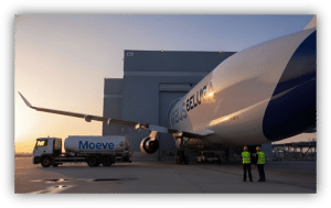 Avión Airbus Beluga estacionado junto a un camión cisterna de Moeve en una plataforma aeroportuaria, con personal y un hangar al fondo durante el atardecer.