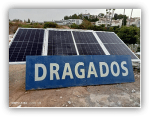 Panel informativo con el nombre Dragados situado frente a una instalación de paneles solares fotovoltaicos sobre una cubierta.