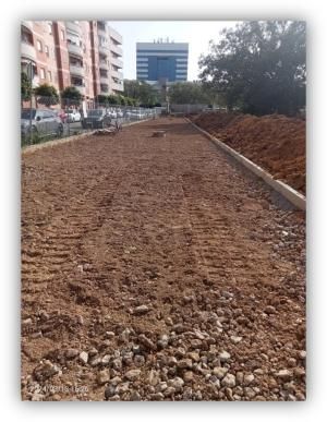 Zona en obras para la creación o mejora de un espacio urbano, con terreno nivelado, bordillos instalados y edificios residenciales al fondo.